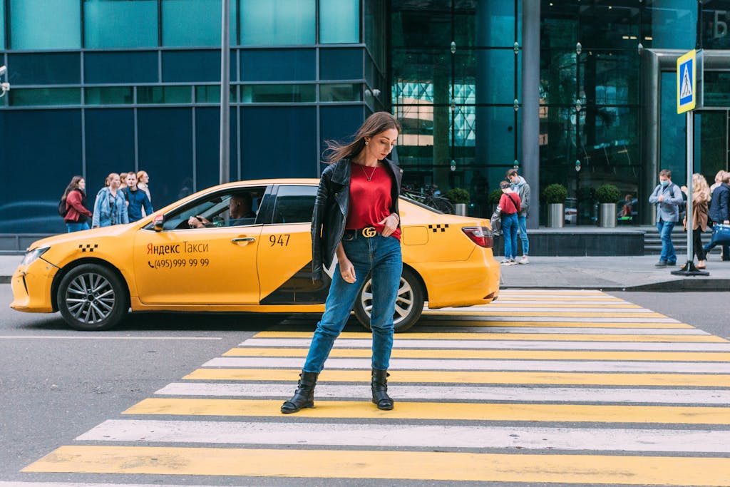Stylish woman crosses pedestrian lane in downtown Moscow with a Yandex taxi in the background.