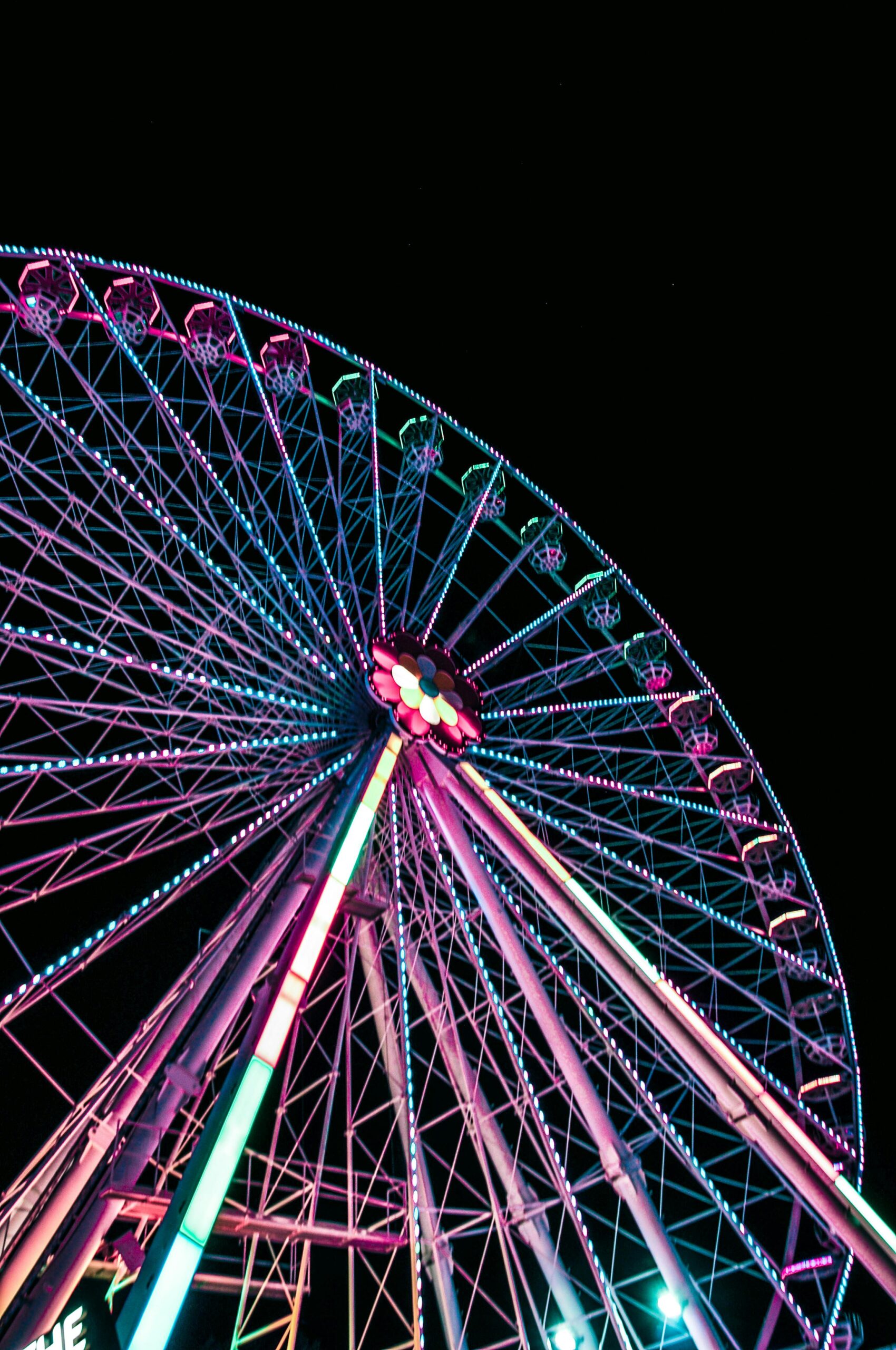 Illuminated Ferris wheel at night in a theme park with vibrant lights