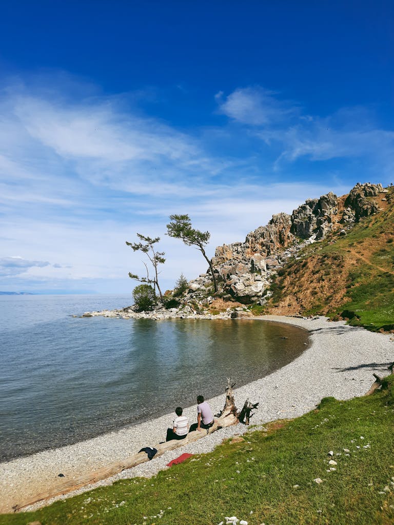 A serene landscape with a couple sitting by the rocky shore of a coastal area in Russia.