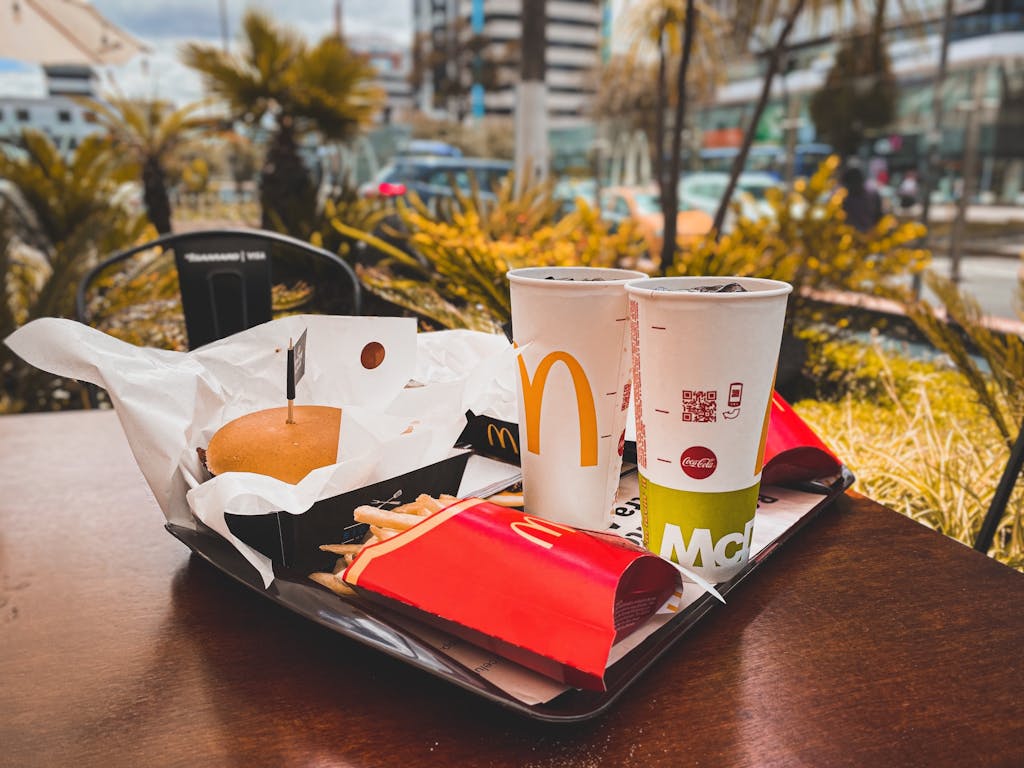 An appetizing fast food meal with burger, french fries, and drinks on an outdoor table in urban setting.