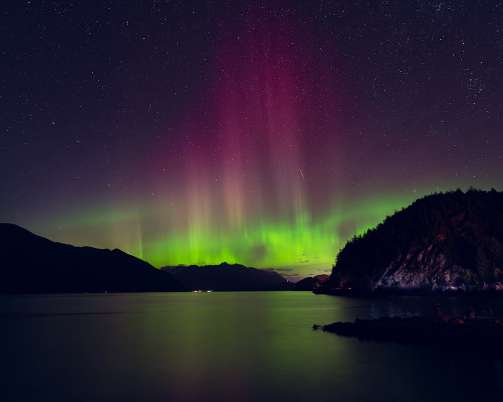 Beautiful northern lights reflecting over a calm lake with a starry sky in the background
